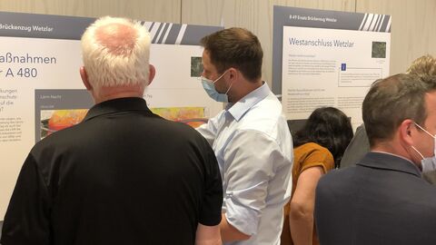 Personen erläutern Besuchern bei der Infomesse Informationen anhand von Infotafeln bei der Infomesse