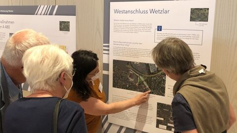 Besucher schauen Informations-Tafeln an einer Wand an, bei der Öffentlichen Infomesse. 