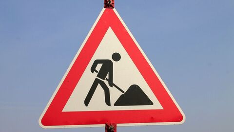 Ein Baustellenschild im Dreick-Format im Detail mit blauem Hinterrund